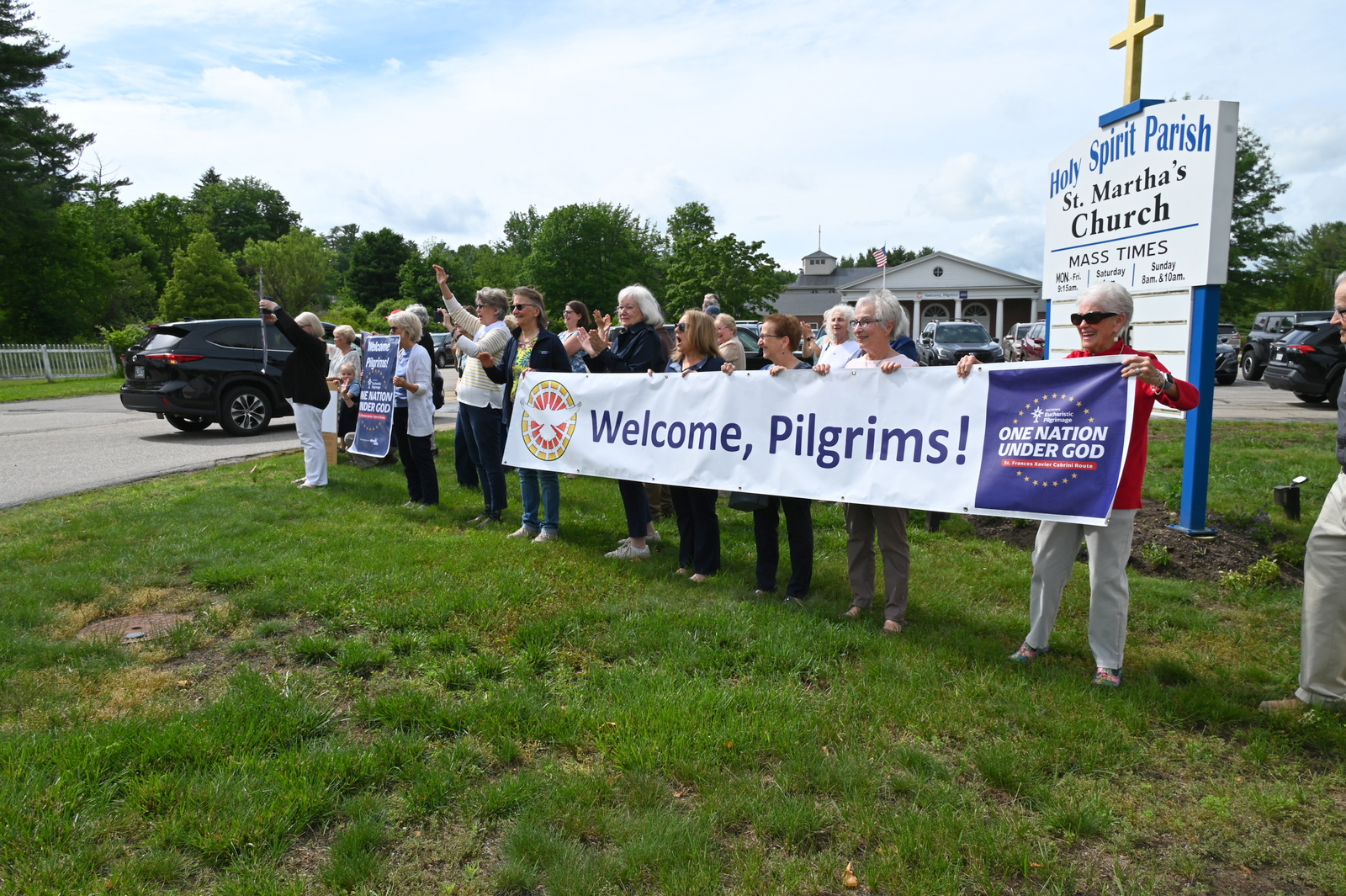 People hold up welcome signs and wave as procession arrives.