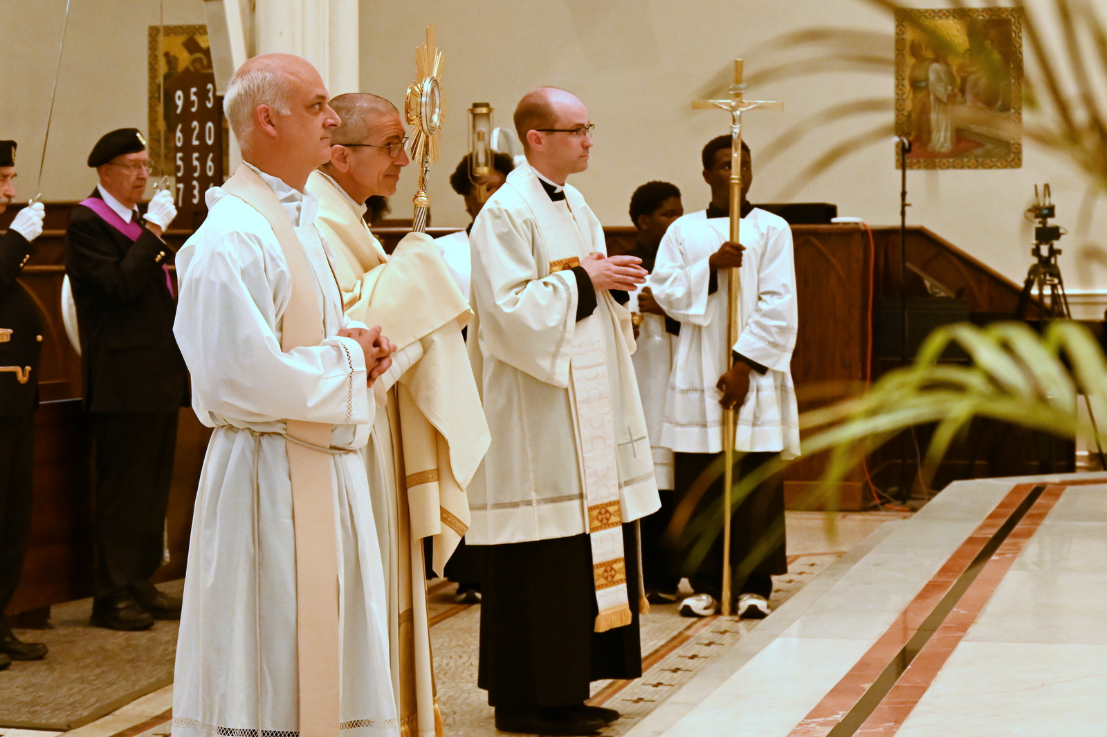 Bishop Ruggieri, carrying the monstrance, Father Jack Dickinson, and Father Seamus Griesbach stand at the foot of the sanctuary.