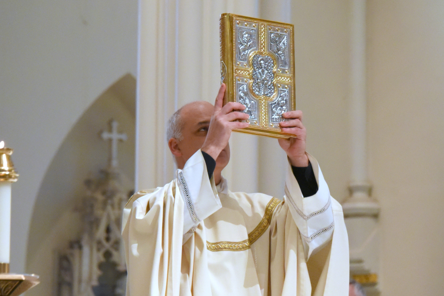 Father Seamus Griesbach holds up the Book of the Gospels.