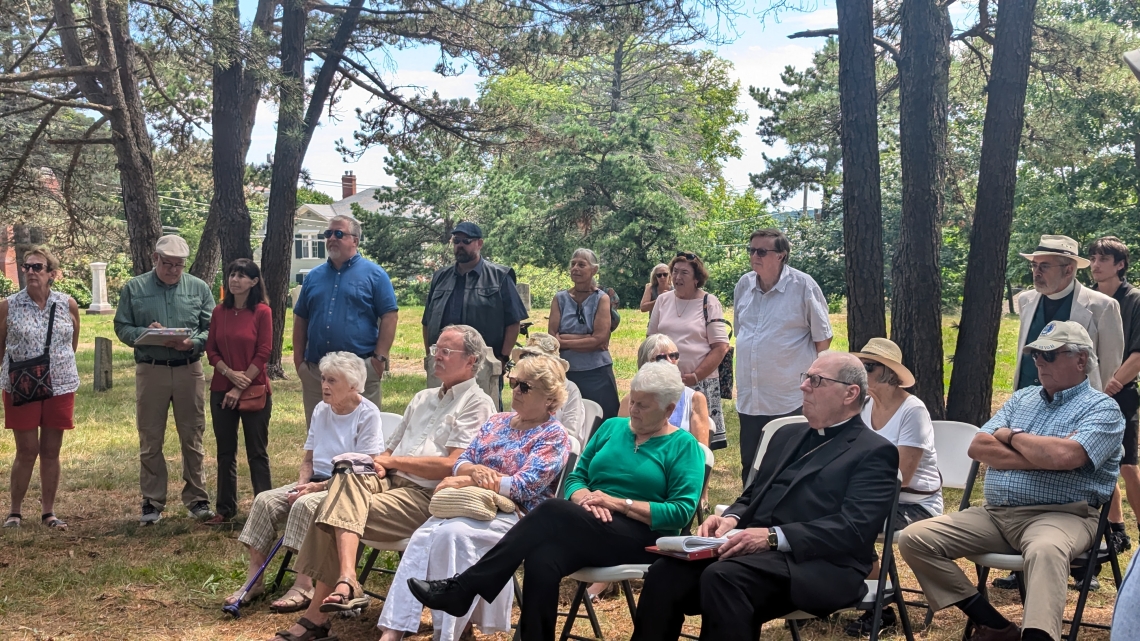 Group sits in a wooded cemetery.