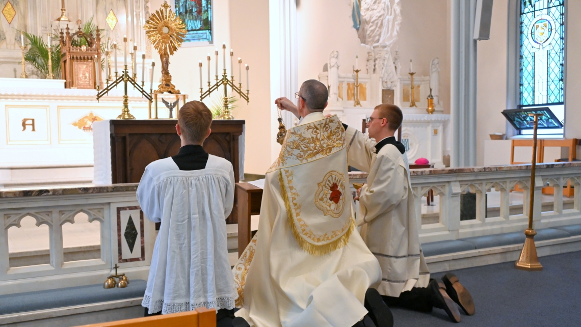 Bishop James Ruggieri incenses the altar and the monstrance. Seminarians Joseph Beale and Nicholas Hershbine are kneeling on either side of him.